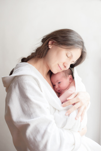 Mother holding newborn in bathrobe at window